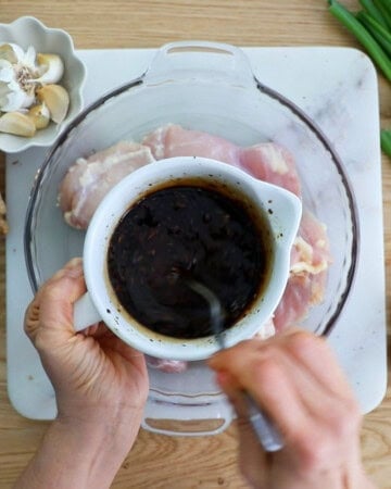 a hand mixing brown teriyaki sauce in a white bowl.