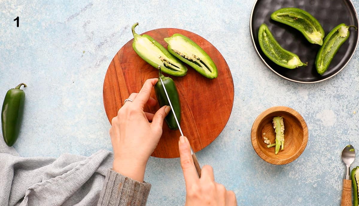two hands slicing one jalapeno pepper in half using a knife.