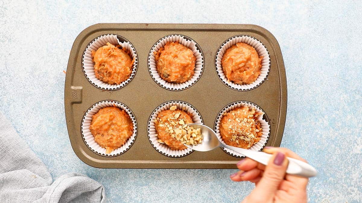 a hand sprinkling chopped walnuts in a muffin pan.