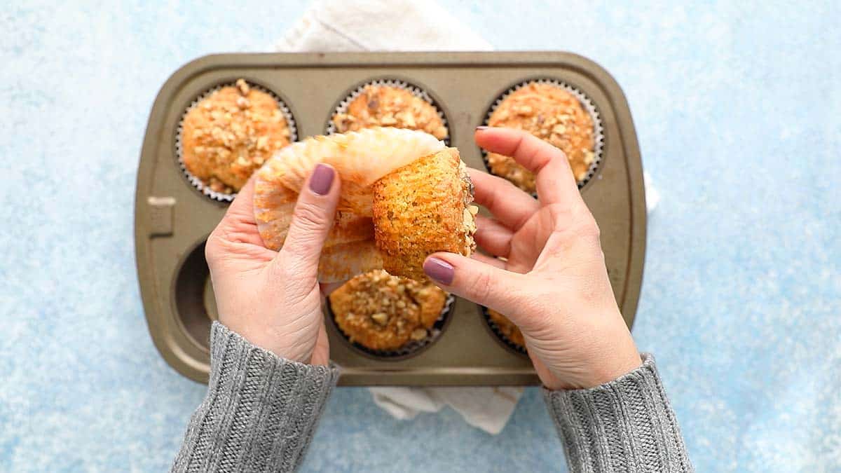 2 hands peeling a carrot muffin.