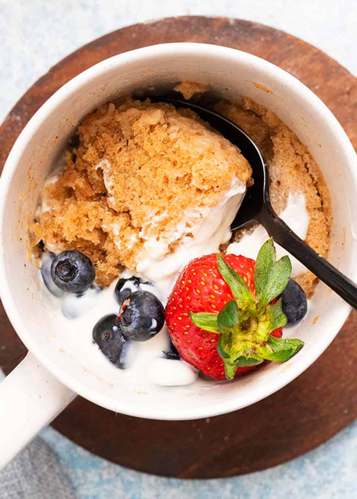 oatmeal mug cake topped with a pink strawberry in a white mug.