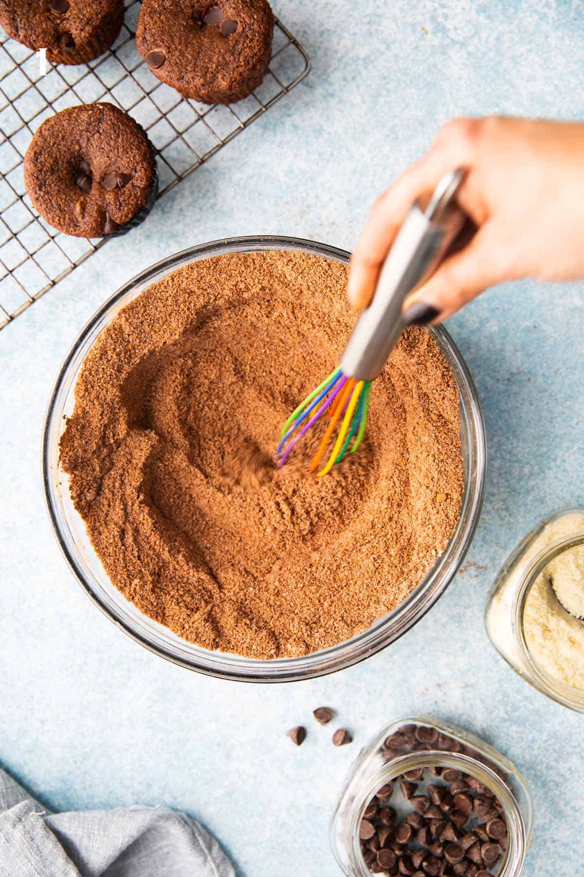 one hand whisking cocoa with flour in a glass bowl.