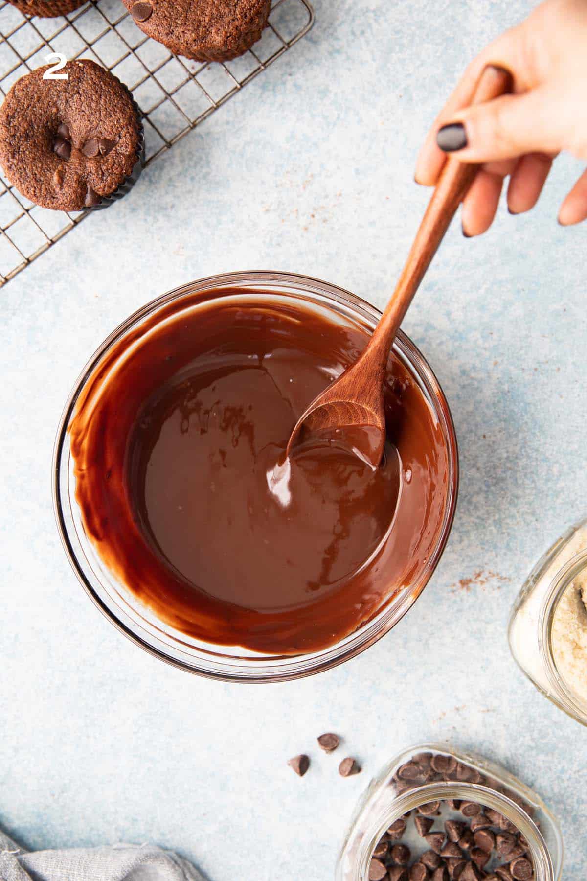one hand mixing melted chocolate in a glass bowl.