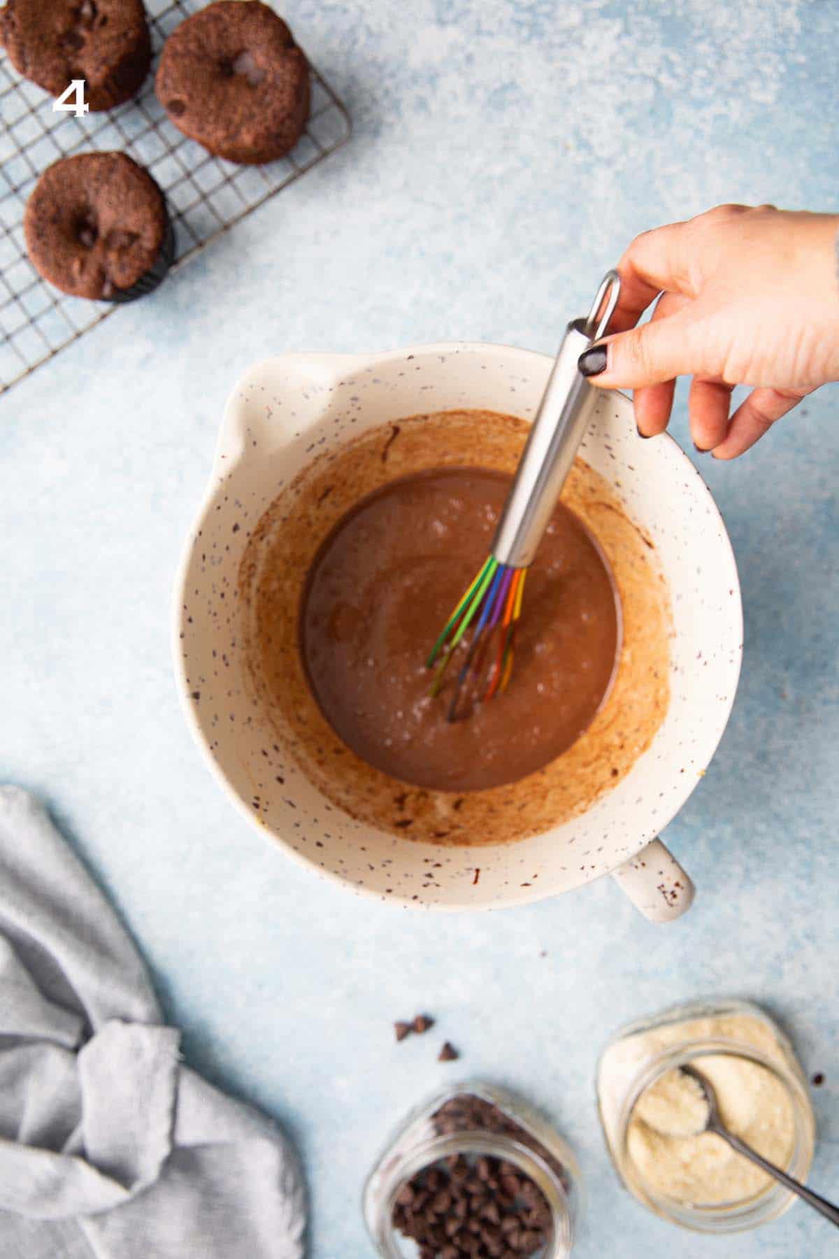 one hand mixing chocolate muffin batter in a large yellow bowl.