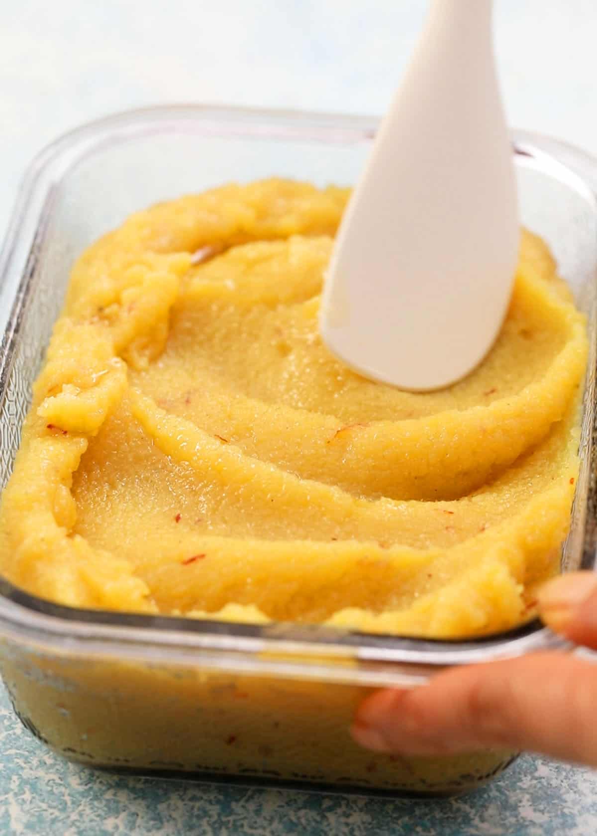 yellow colored badam halwa in a glass dish.