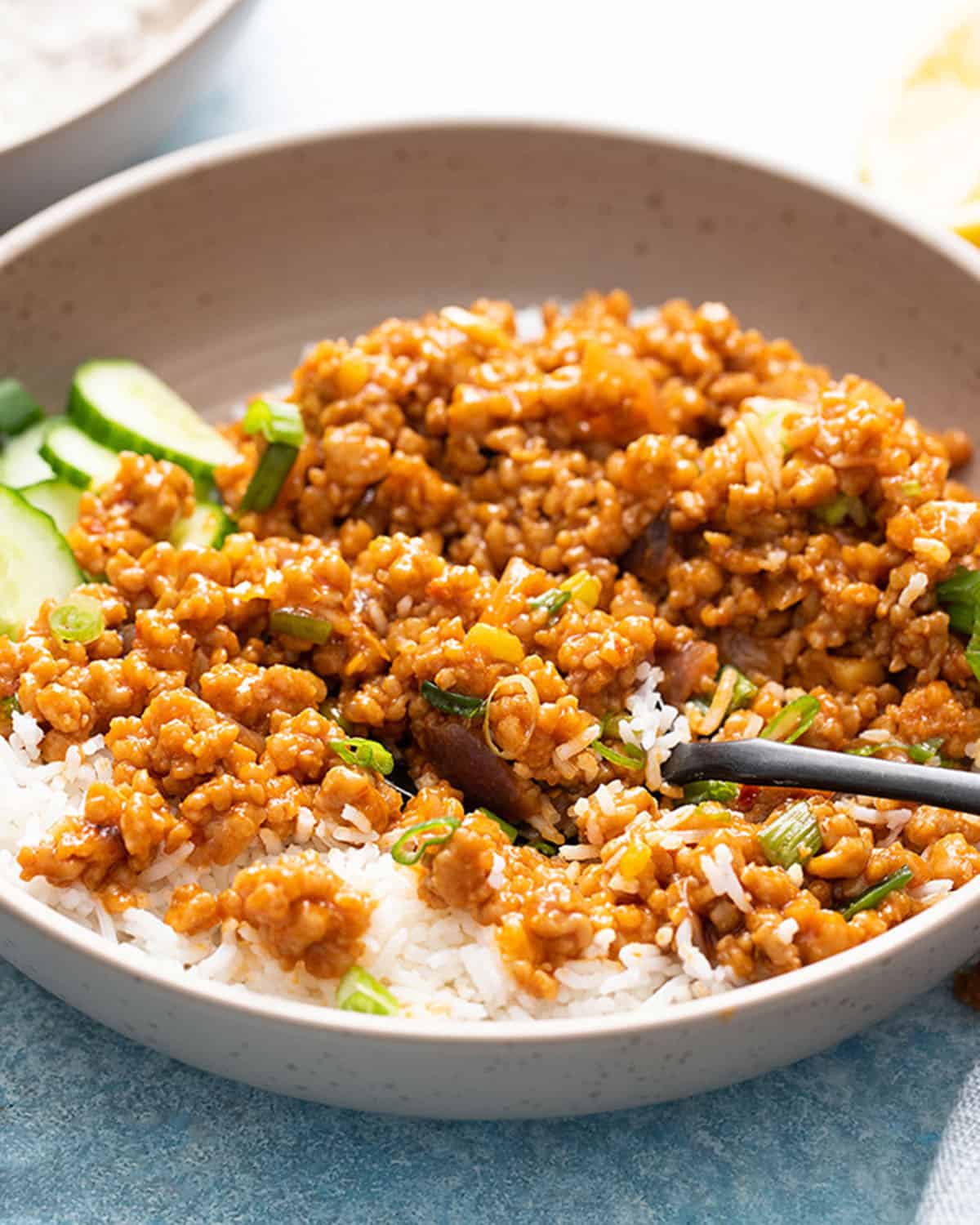 brown ground chicken stir fry along with white rice in a brown bowl along with a black fork.