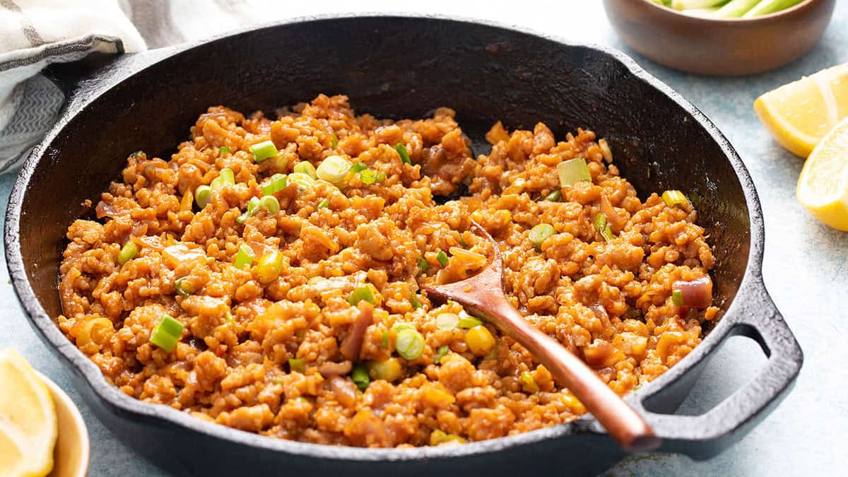 ground chicken stir fry in a black skillet along with a wooden spoon.
