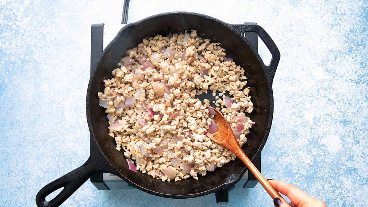 a hand cooking ground chicken and chopped onions in a black skillet.