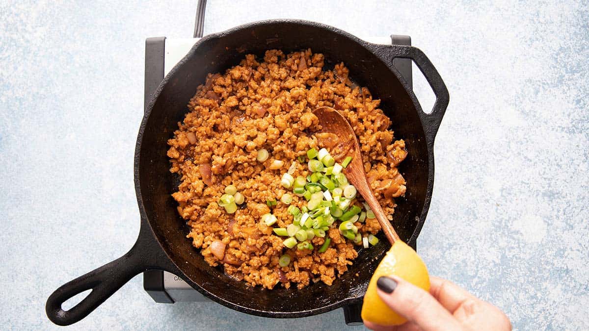 a hand cooking ground chicken and chopped onions in a black skillet.