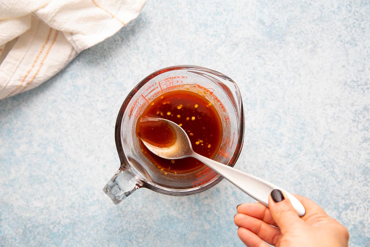 stirring sriracha honey sauce in a measuring cup with spoon. 