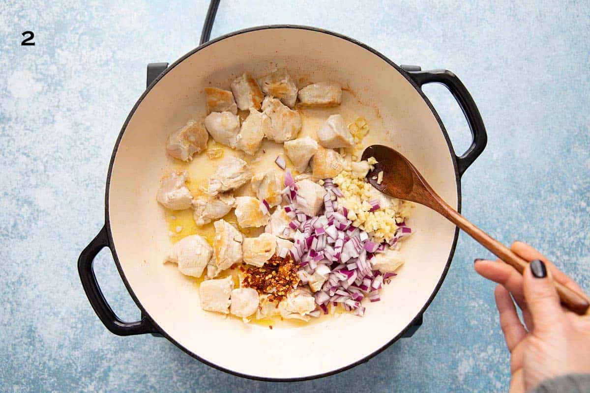 a hand sautéing  cooked chicken pieces, chopped onion and garlic in a large white skillet.