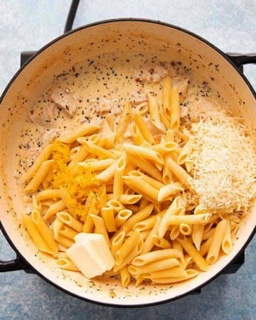cooked yellow penne pasta, white parmesan cheese and butter in a large white pan.
