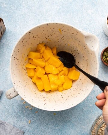 a hand mixing chopped mangocubes in a large white cup.