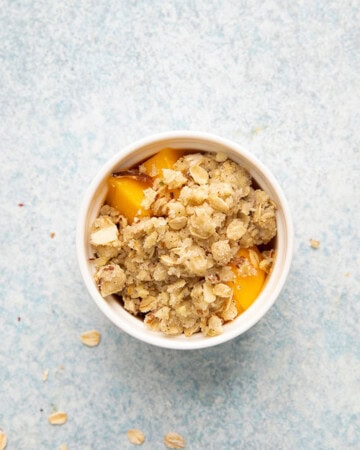 one white baking cup with chopped mango cubes topped with crumble topping.