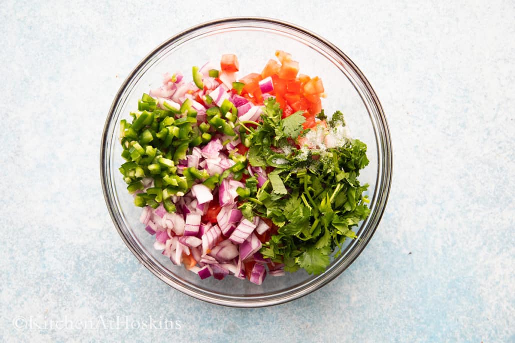 a glass bowl with all ingredients needed to make pico de gallo. 