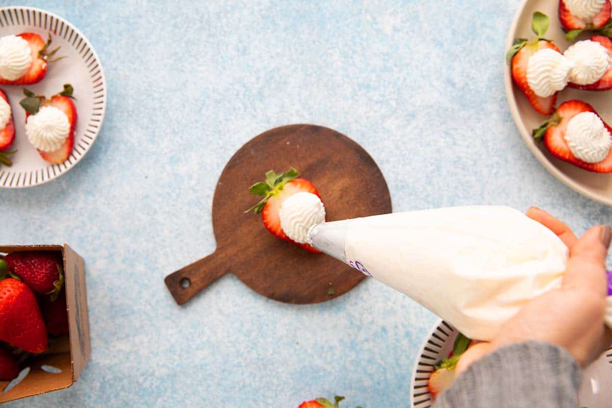 PIPING WHIPPED CREAM ON TOP OF A STRAWBERRY HALF.