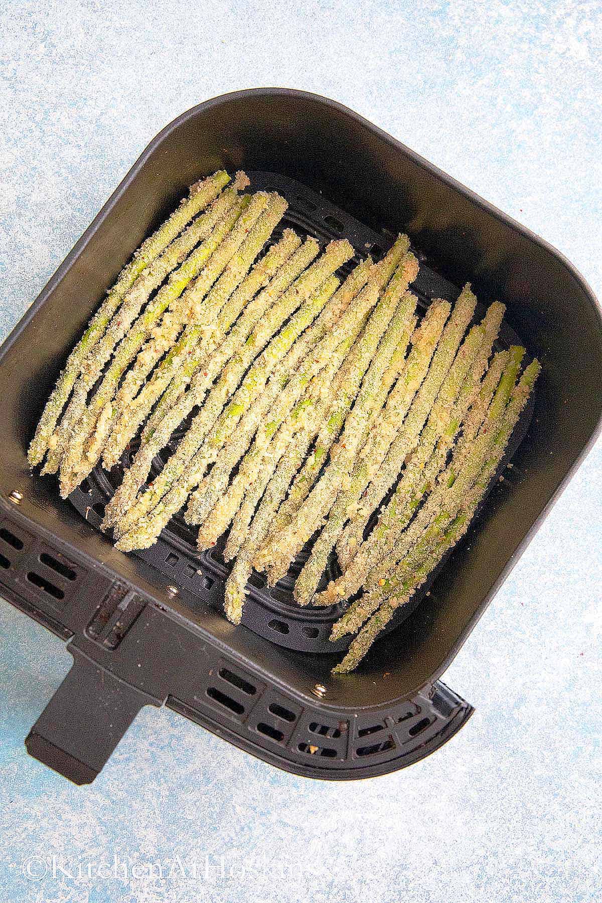 air fryer basket with breaded asparagus.