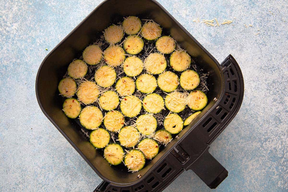 sliced zucchini rounds topped with parmesan cheese in an air fryer basket.