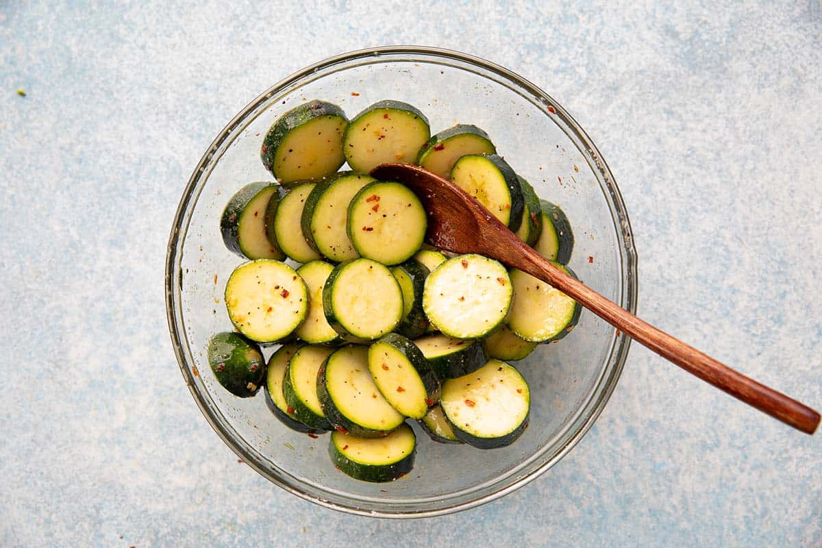 cut zucchini discs mixed with olive oil and spices in a glass bowl. 