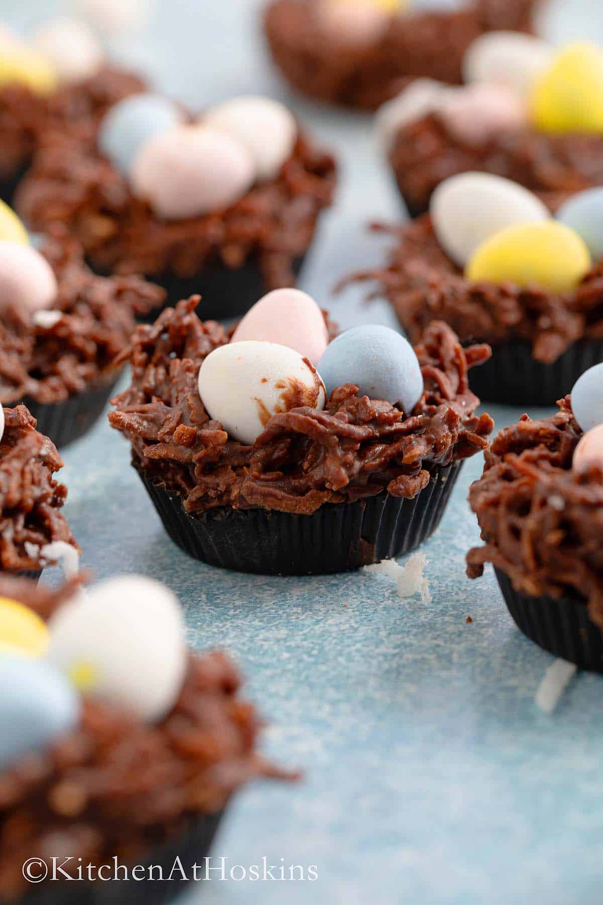 Chocolate nests with candy eggs on a blue board.