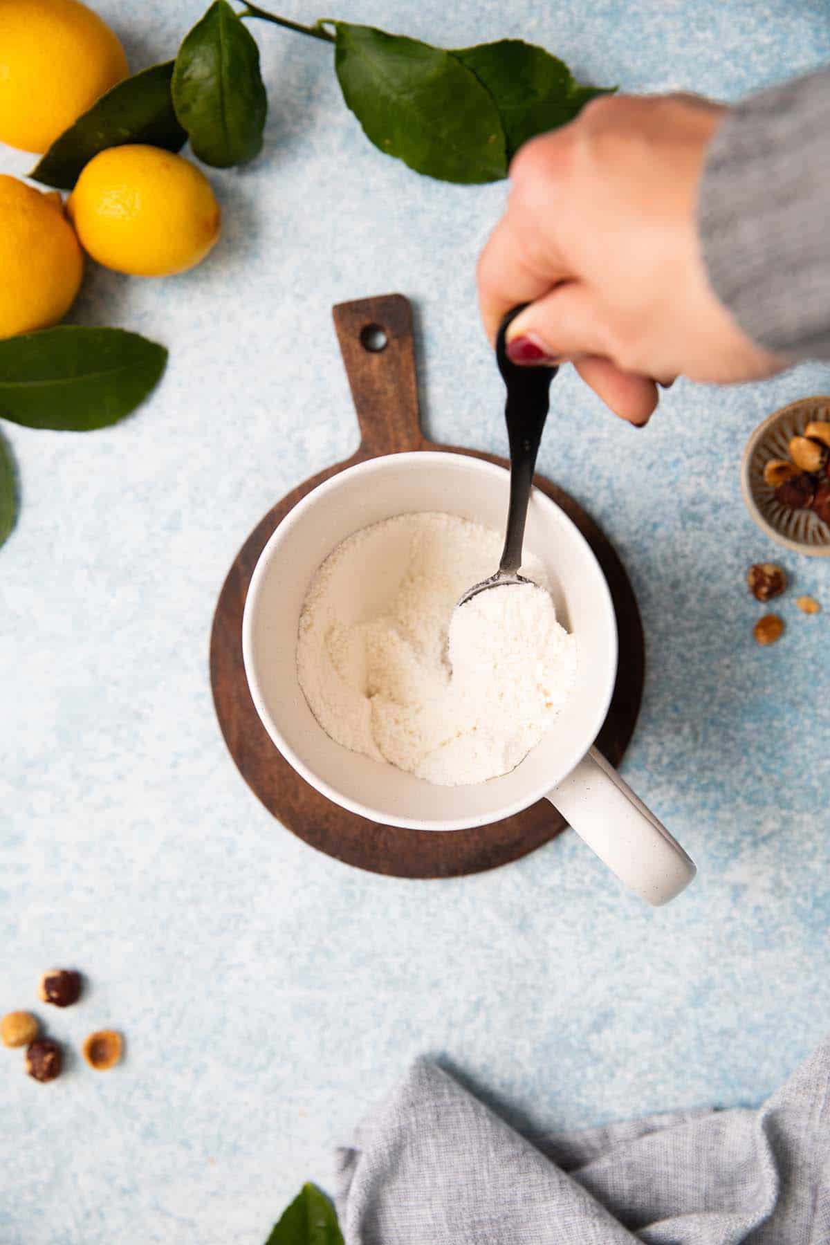 a hand stirring white flour in a white mug using a black spoon. 