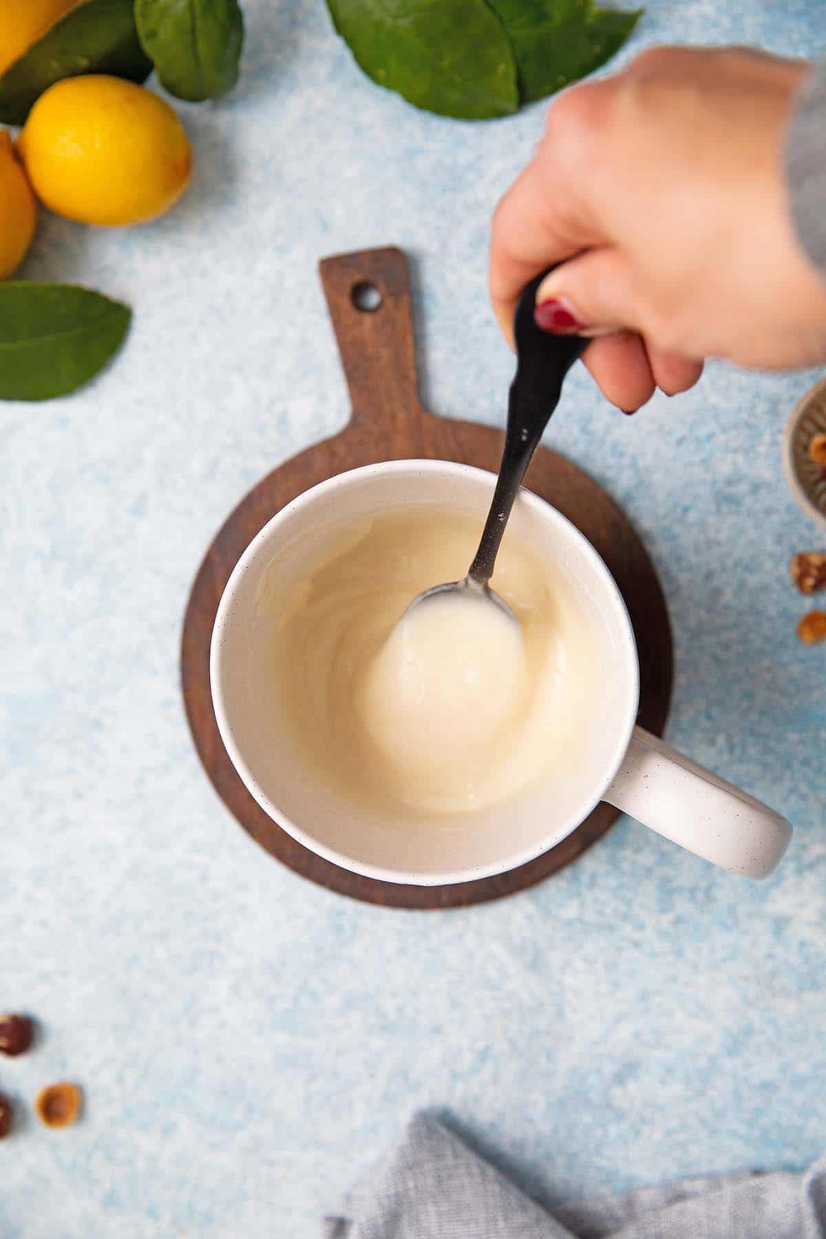 a hand stirring cake batter in a white mug using a black spoon. 