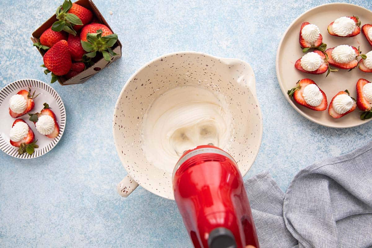 BEATING GREEK YOGURT AND CREAM WITH A RED ELECTRIC BEATER.