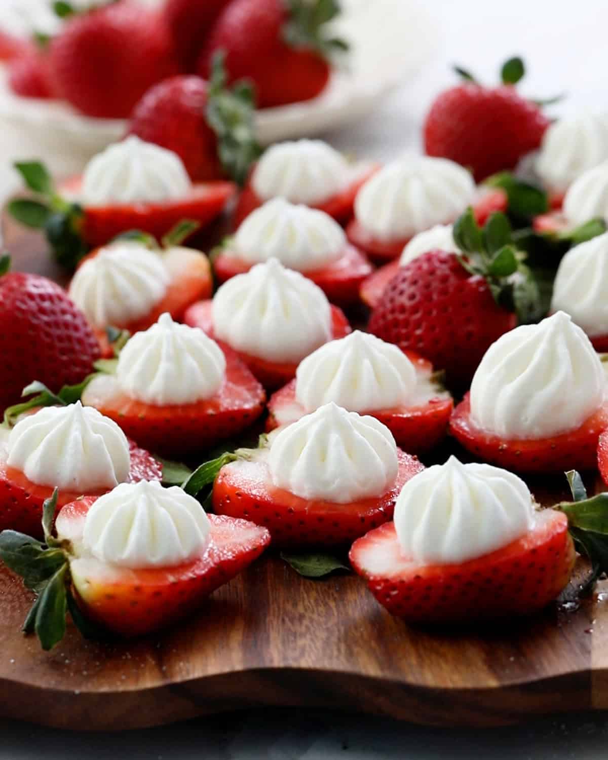 red strawberries toped with white cream placed on a brown board.
