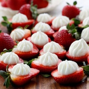 red strawberries toped with white cream placed on a brown board.