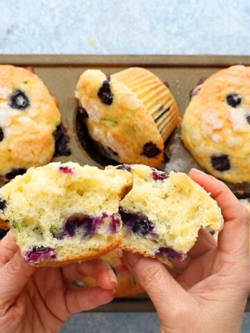 two hands holding two split halves of a blueberry muffin.