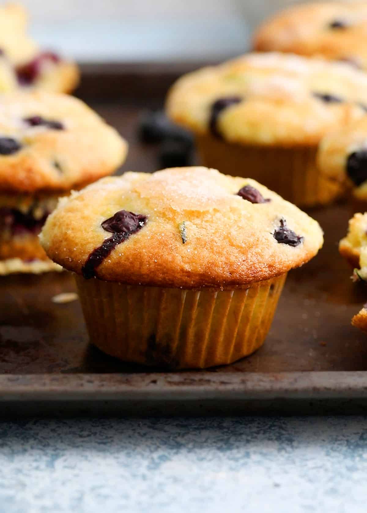 5 blueberry lemon muffins placed on a metal sheet tray.