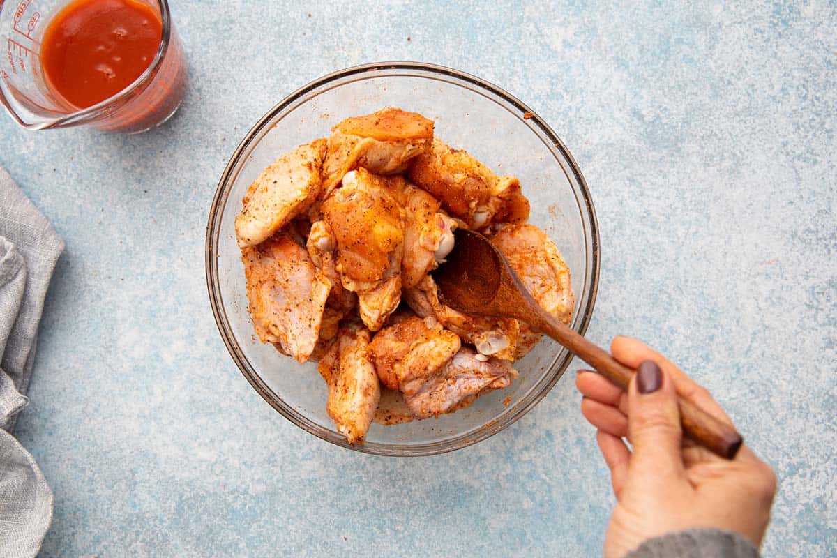 mixing chicken wings with seasoning in a glass bowl. 