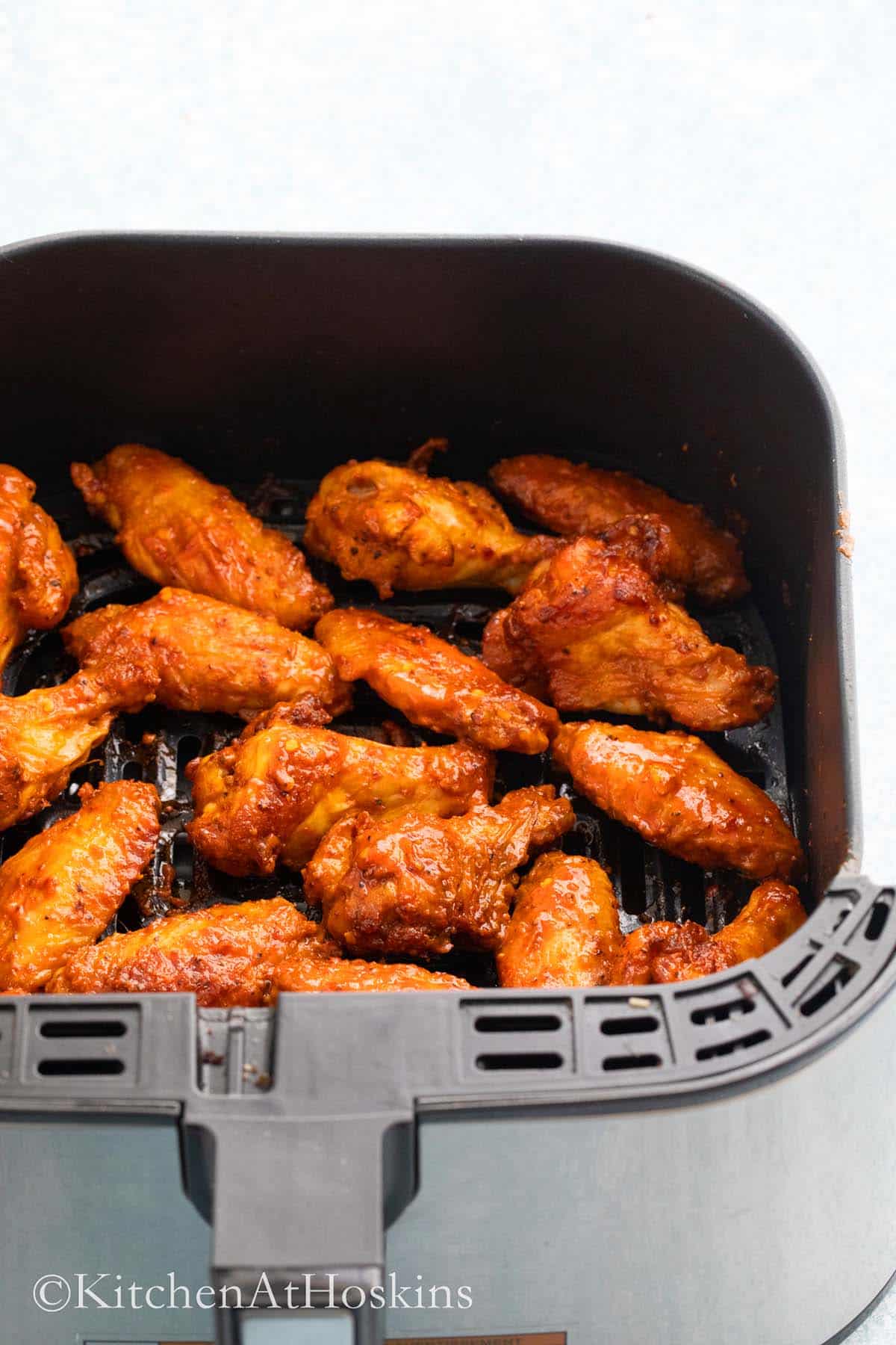 spicy wings tossed in buffalo sauce in an air fryer basket.
