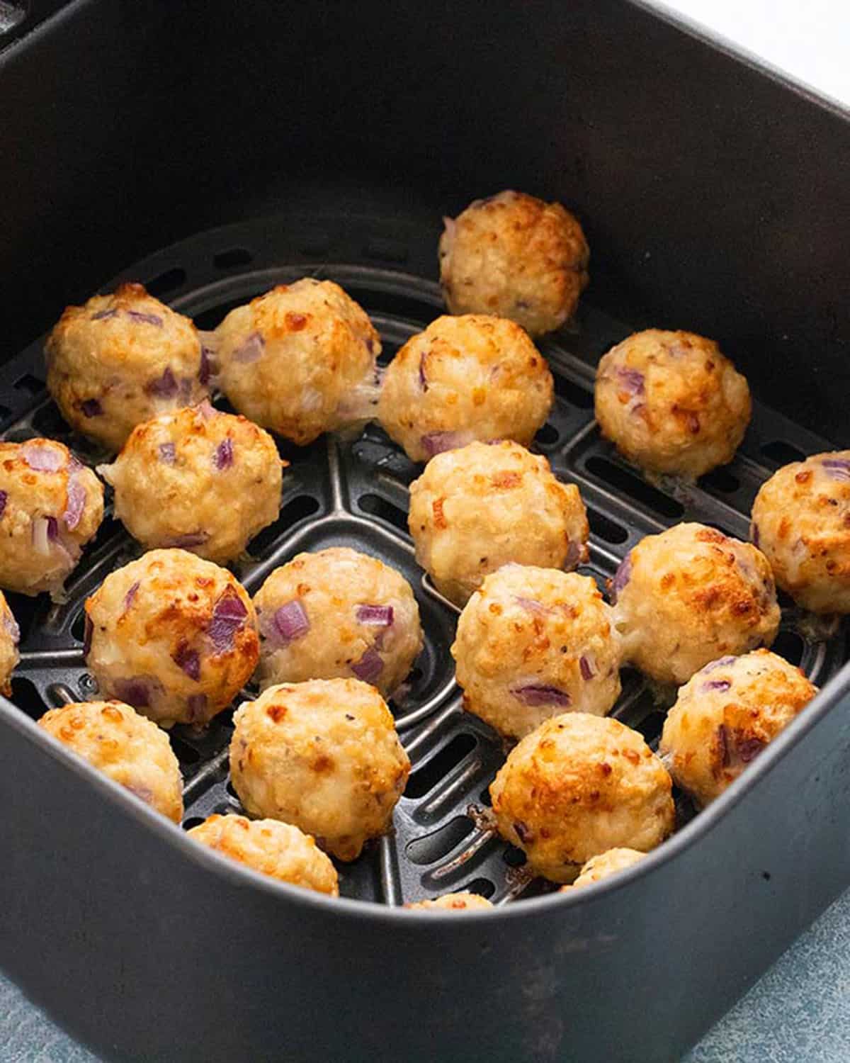cooked chicken meatballs in an air fryer basket.