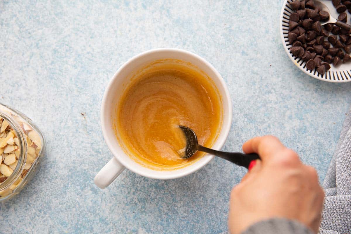 stirring almond flour, egg and brown sugar in a white mug.