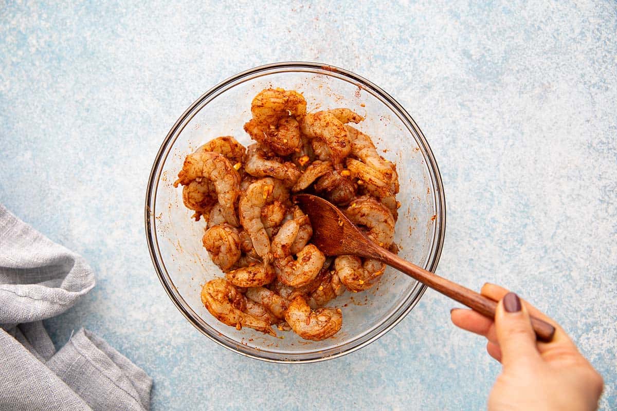 tossing shrimp with spices in a glass bowl. 