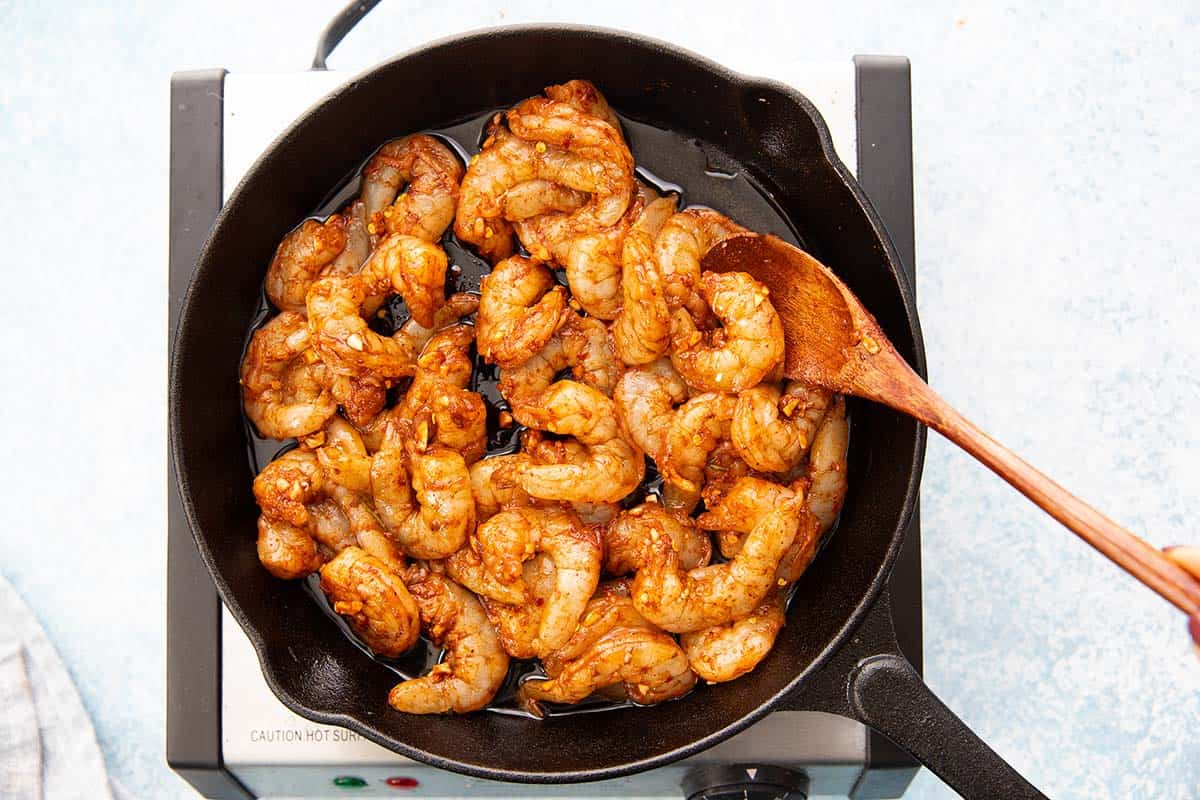 stir frying shrimp and spices in a cast iron skillet.