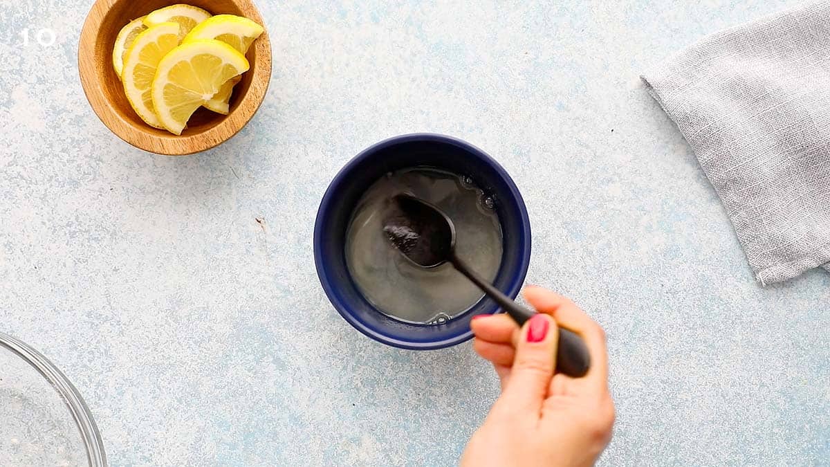 a hand mixing sugar and lemon juice in a blue bowl with a black spoon.