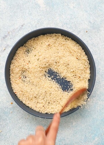 a hand mixing panko breadcrumbs in a blue plate.
