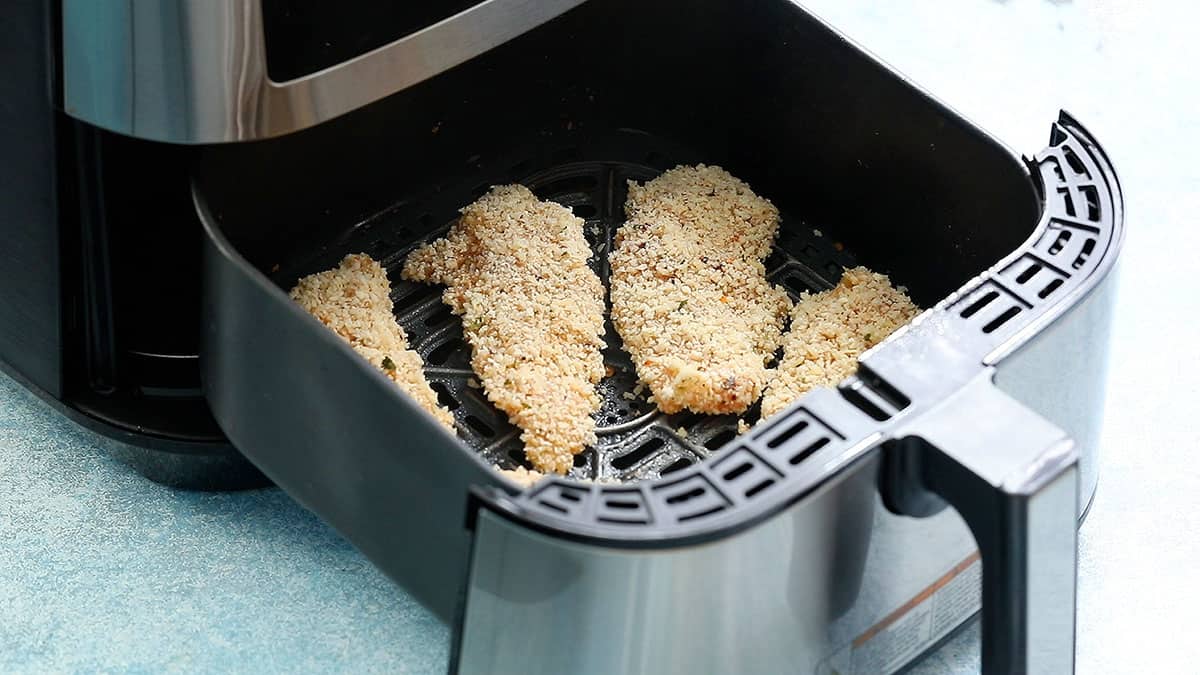 breaded chicken tenderloins in an air fryer basket.