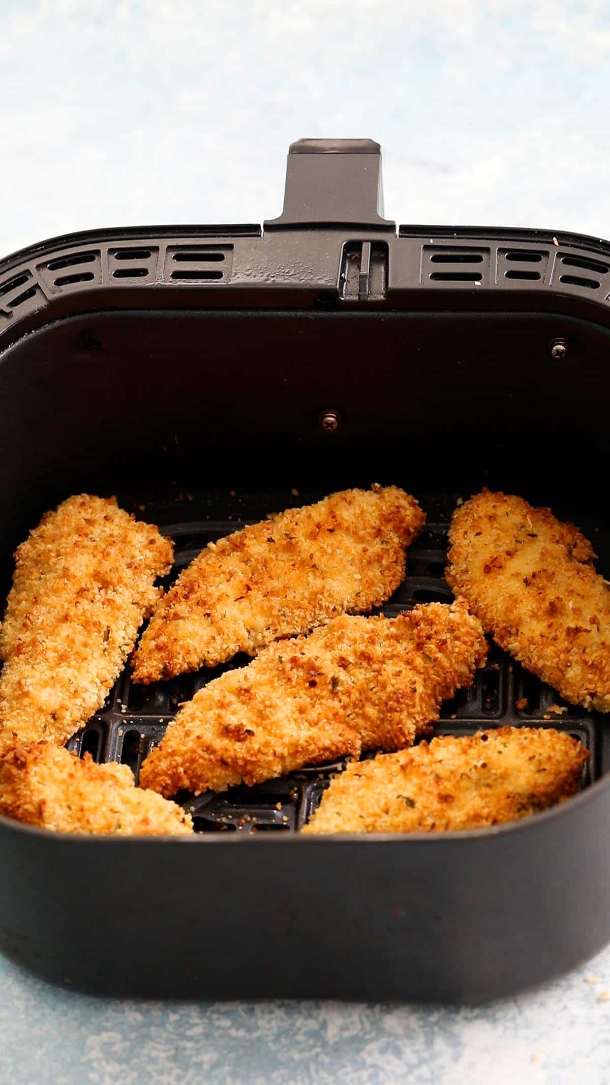 breaded chicken tenders in an air fryer basket.