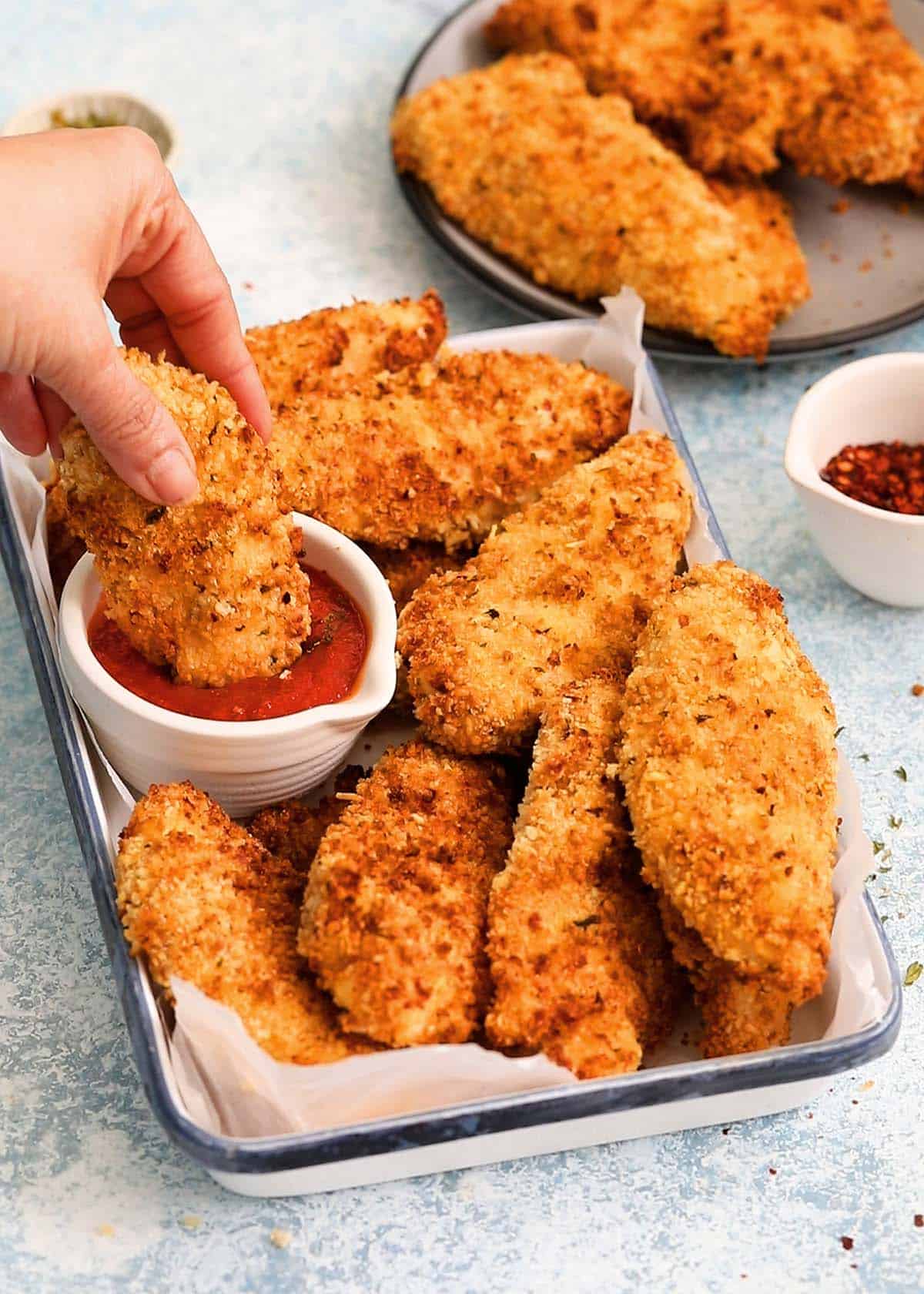 a hand dipping one breaded chicken tender in tomato sauce.