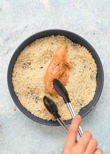 a hand coating a chicken tenderloin in breadcrumbs.