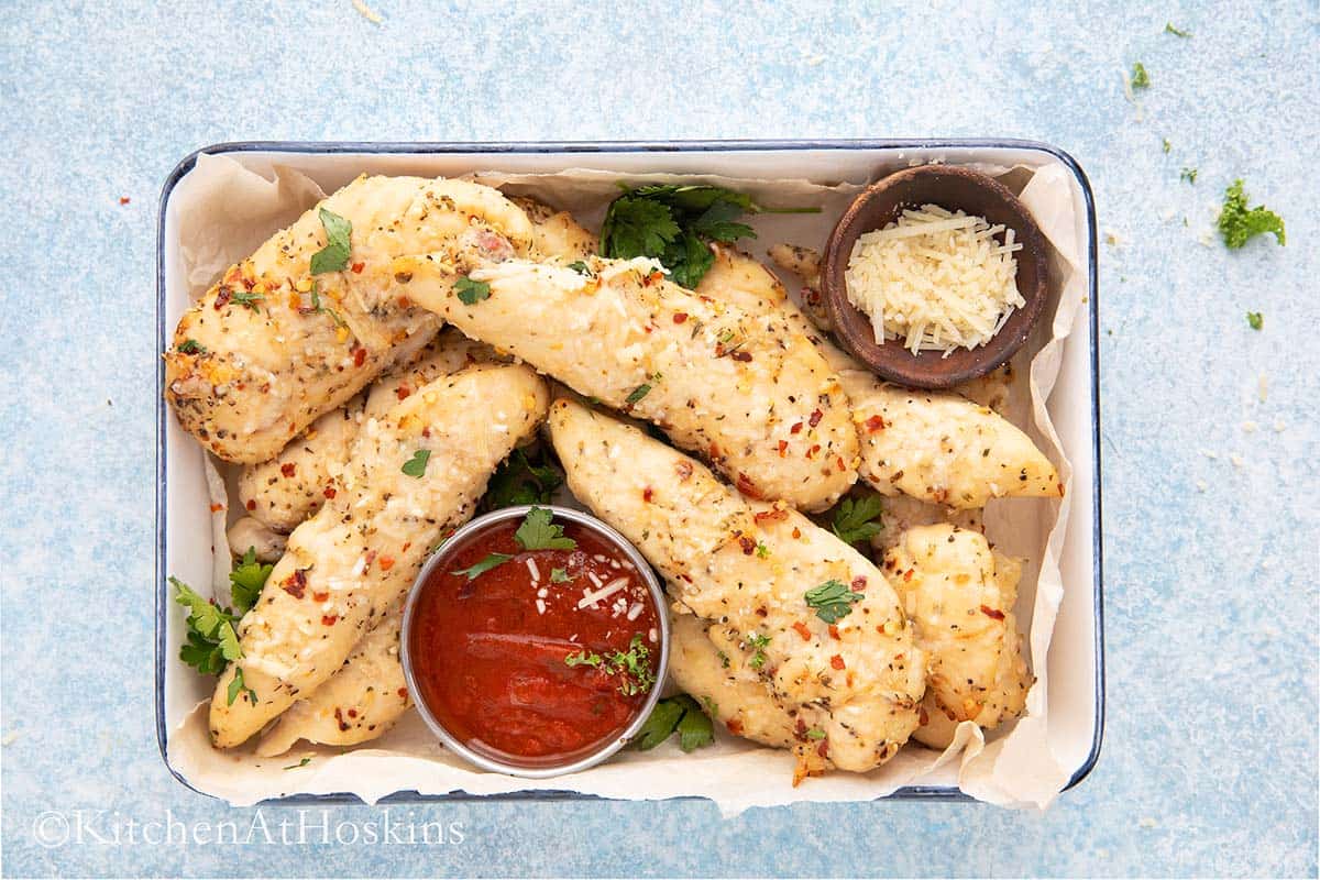 cooked garlic parmesan tenders in a tray with sauce for dipping.