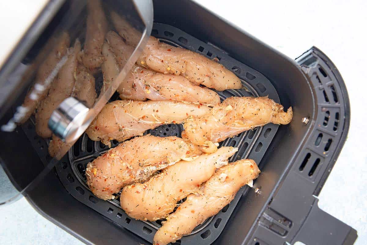 marinated chicken tenders in an air fryer basket.