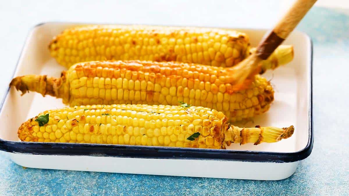 3 cooked corn on the cobs in a white tray.