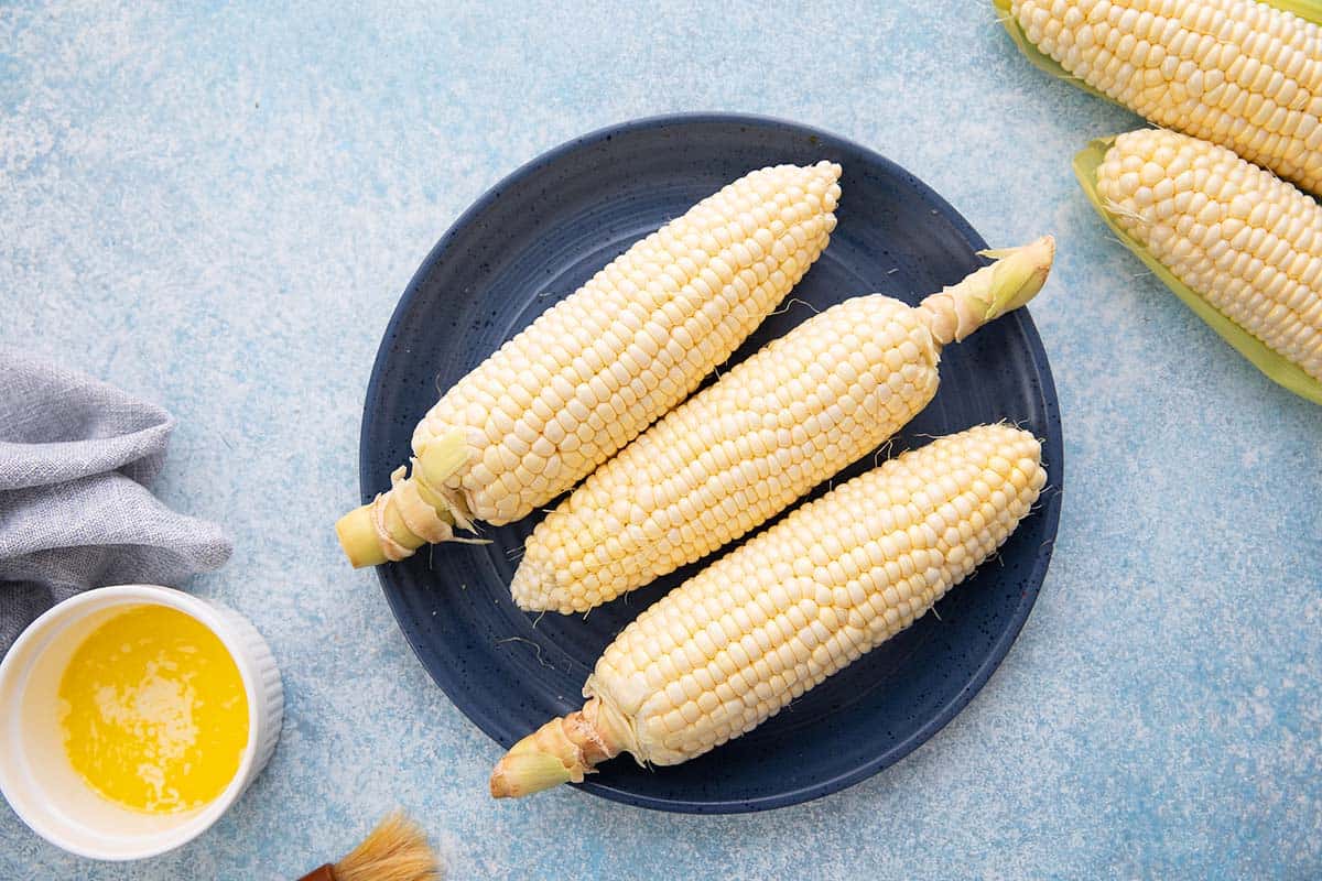 Air fry corn on the cob in husk 2 3 corn on the cob on large blue plate.