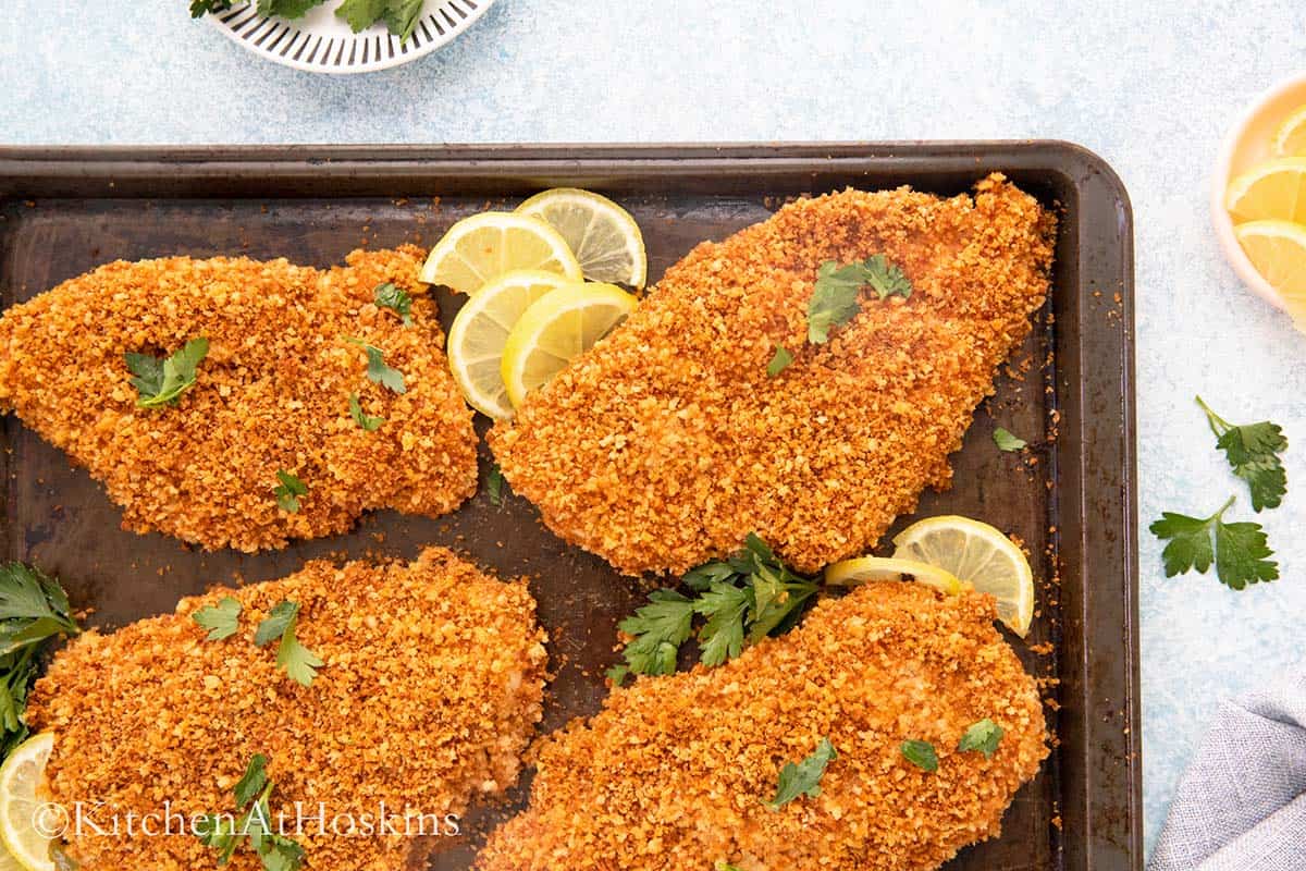 breaded chicken in a baking pan with lemon slices.