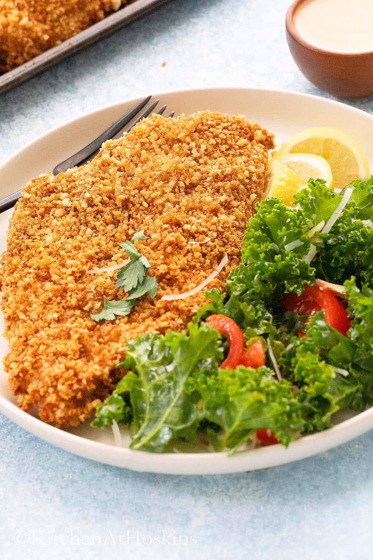 white plate with crispy chicken along with kale salad.