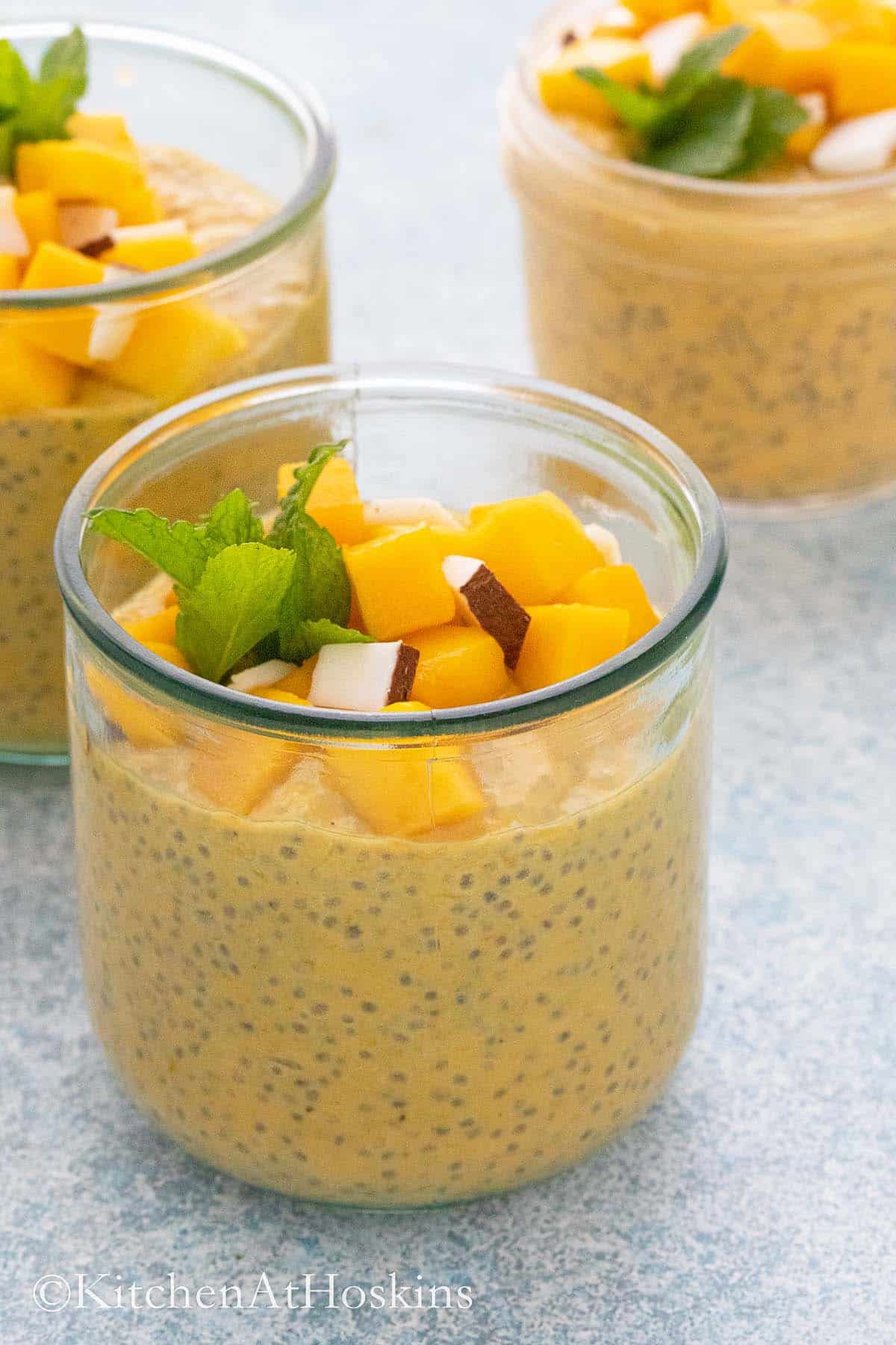 three glass cups filled with yellow mango chia pudding.